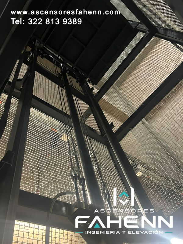 Sistema de guías y cadenas para ascensor de carga instalado dentro de una estructura metálica con malla.