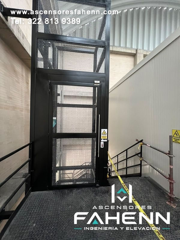Torre de elevación para carga pesada con cerramiento de malla, puerta metálica y plataforma antideslizante.