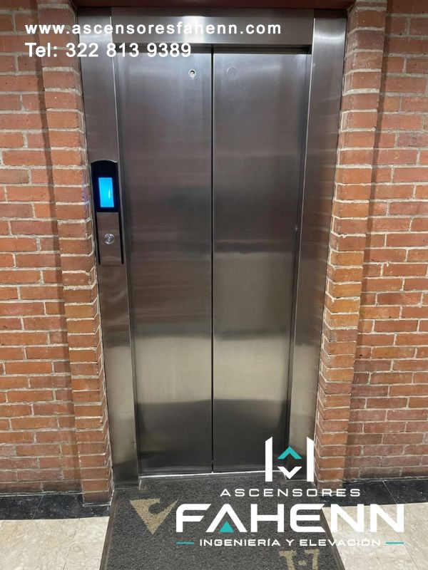 Puertas para ascensores en acero inoxidable con apertura central, encuentro alineado de dos hojas y estación lateral con pantalla luminosa azul.