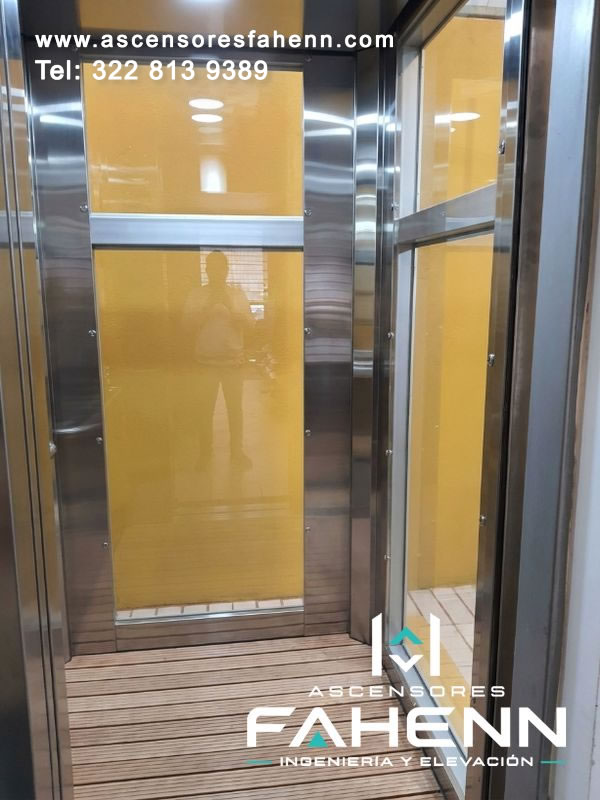 Cabina compacta con revestimientos amarillos, vidrio lateral, remates de acero y superficie de piso con líneas que reproducen una apariencia de madera.