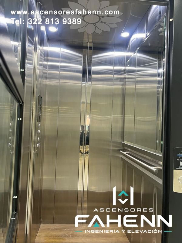 Cabina de lujo con espejos de gran altura, figura floral en el techo, iluminación empotrada, pasamanos de acero y superficie de piso amaderada.