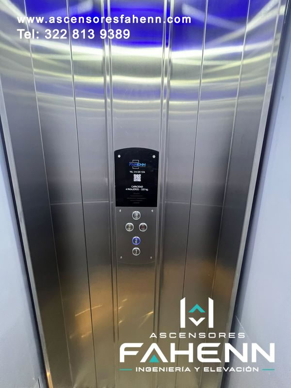 Interior de elevador compacto con paneles metálicos, botonera para cuatro pasajeros y selección activa identificada mediante un aro luminoso azul.