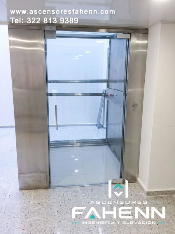 Cabina panorámica acristalada con puerta abierta, estructura de acero y superficies transparentes que reciben abundante iluminación del corredor.