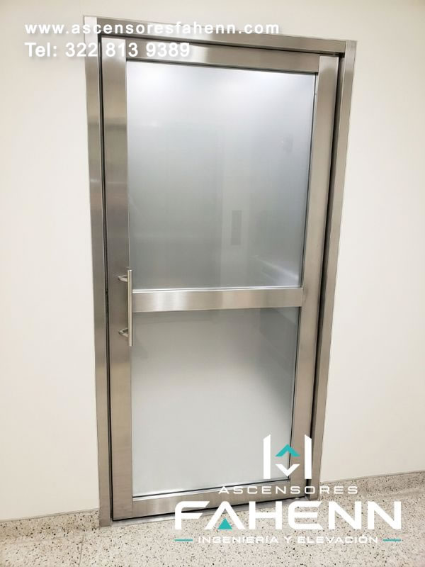 Puerta de ascensor con vidrio esmerilado, perfiles de acero pulido y manija metálica que conserva privacidad visual en un corredor de tonos claros.