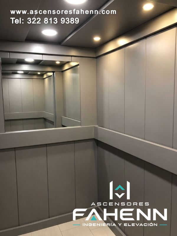 Cabina de ascensor con revestimientos grises, espejo panorámico y luces empotradas blancas y cálidas que crean una atmósfera interior serena.