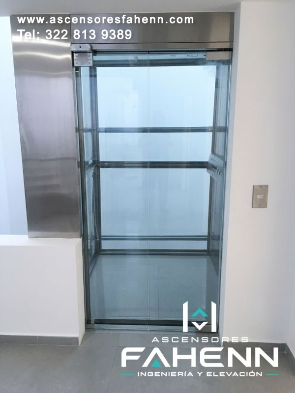 Cabina panorámica de vidrio visible desde el corredor, enmarcada por perfiles de acero y equipada con superficies transparentes de gran altura.