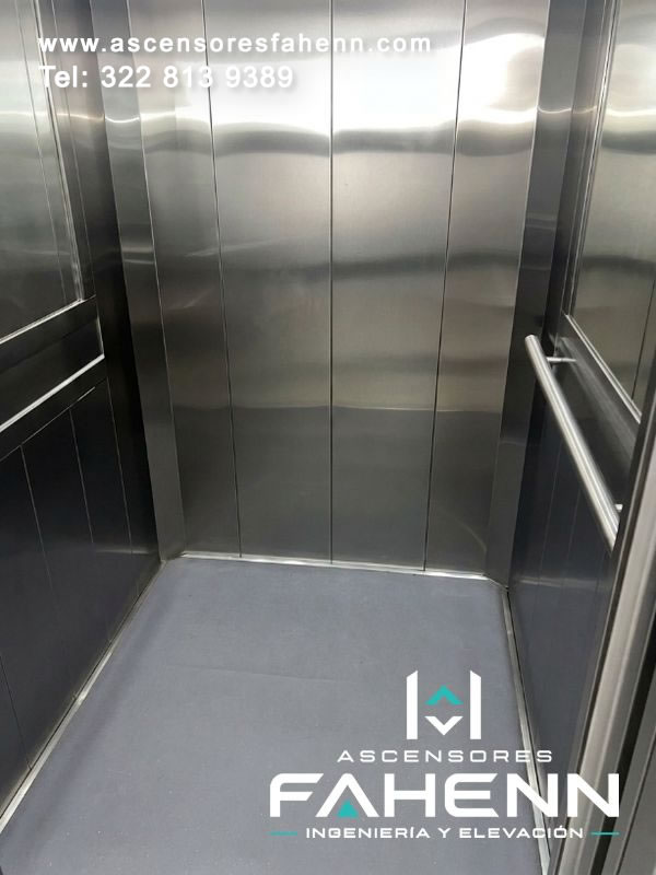 Cabina interior de ascensor con paredes reflectivas de acero, pasamanos tubulares a ambos lados, juntas verticales y superficie de piso uniforme para un viaje cómodo.