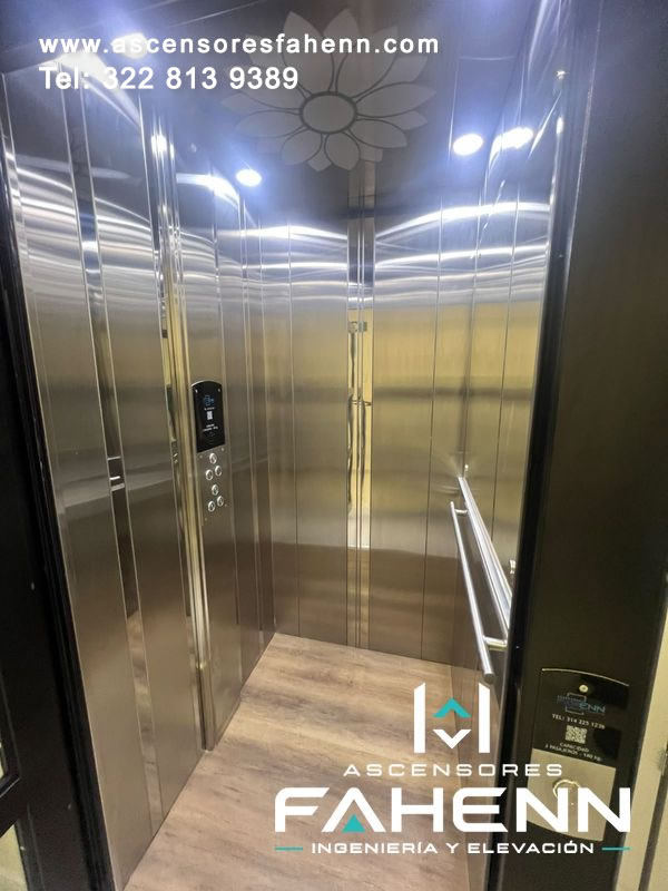 Cabina de lujo en acero reflectivo con botonera vertical, pasamanos metálico, focos superiores, motivo floral y piso de apariencia amaderada de acabado elegante.