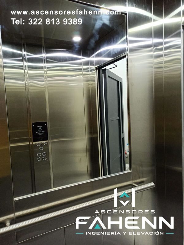 Cabina de ascensor con espejo amplio, acero inoxidable brillante, pasamanos metálico doble, botonera reflejada e iluminación superior moderna.