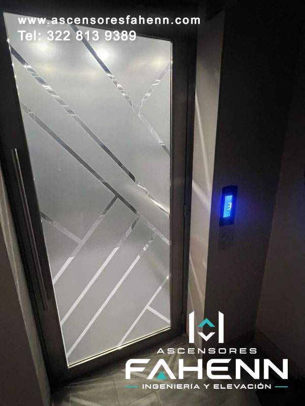 Puerta esmerilada de ascensor con diseño de líneas diagonales, marco oscuro, manija vertical y control digital exterior que indica el piso 3.