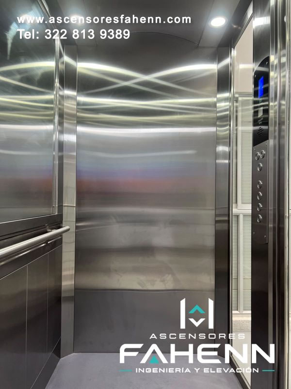 Cabina elegante de ascensor con acero inoxidable, espejo lateral, pasamanos doble, luces LED, botonera digital y piso gris uniforme.