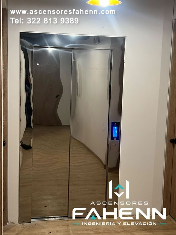 Ascensor para casa con puertas automáticas espejadas, marco metálico, pantalla de piso 3 y acabado reflectivo integrado a un corredor residencial.
