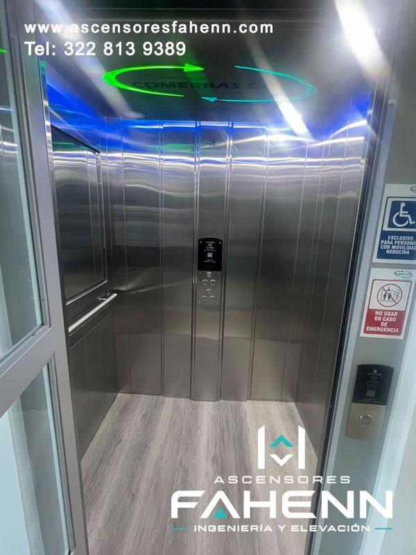 Ascensor para personas con movilidad reducida con cabina de acero, espejo lateral, luces LED azules, controles centrales y piso tipo madera.