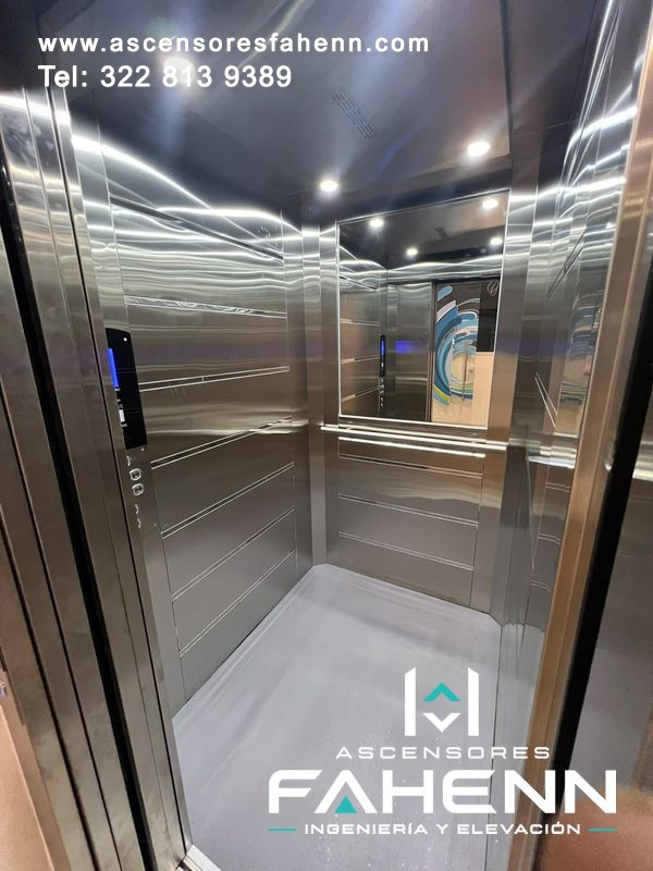 Cabina espejada de ascensor de lujo con acero inoxidable brillante, espejo posterior, pasamanos, controles digitales y piso gris.