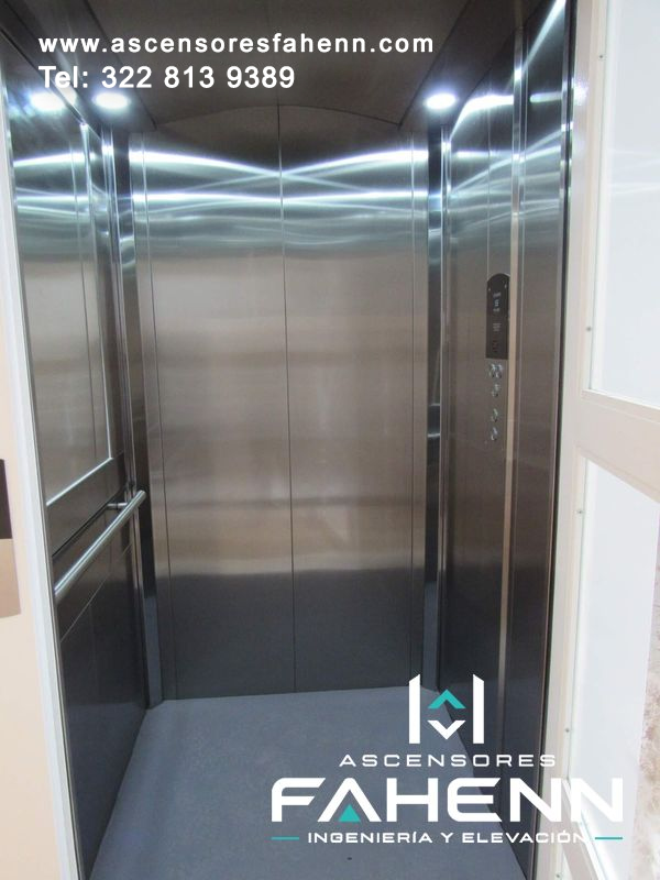 Ascensor para casa con cabina de acero inoxidable, puertas centrales, espejo lateral, pasamanos, controles a la derecha e iluminación LED.
