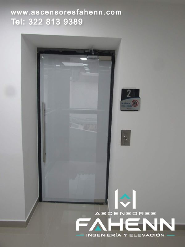 Puerta esmerilada de ascensor con marco oscuro, tirador metálico, mecanismo superior y señal lateral que identifica el segundo piso.