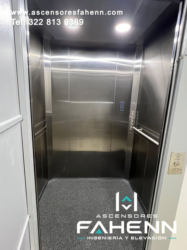Cabina de ascensor en acero inoxidable con piso antideslizante, pasamanos laterales, botonera y luz LED circular.
