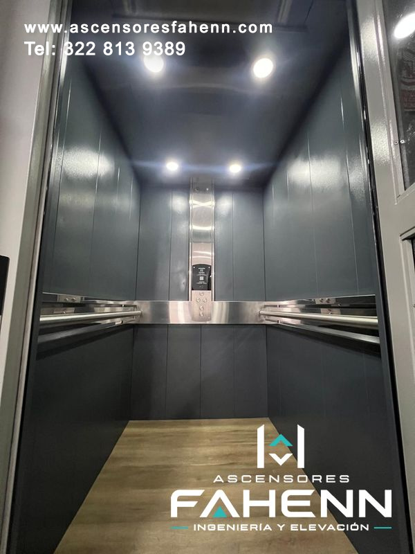 Elevador residencial con cabina amplia, paneles grises, pasamanos dobles, cuatro luces LED y piso tipo madera.