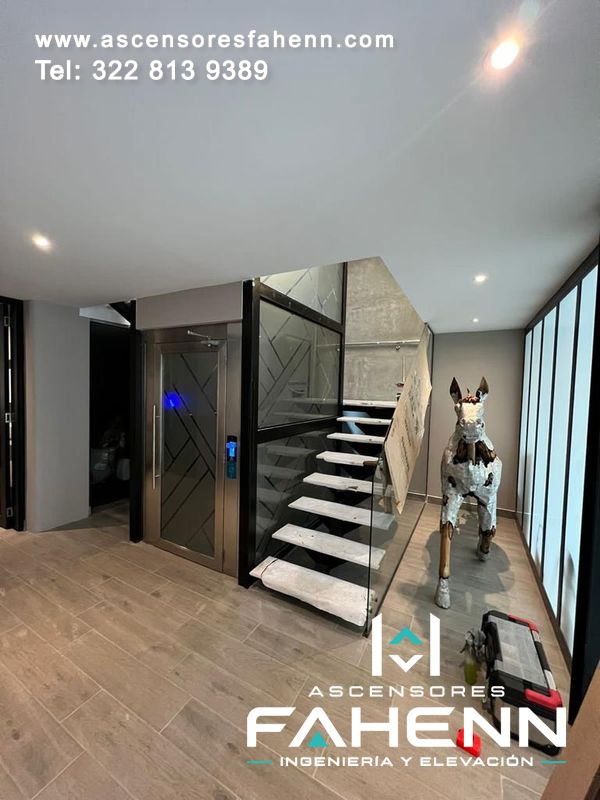 Ascensor para casa con puerta de vidrio oscura, botonera digital azul e instalación junto a una escalera moderna.