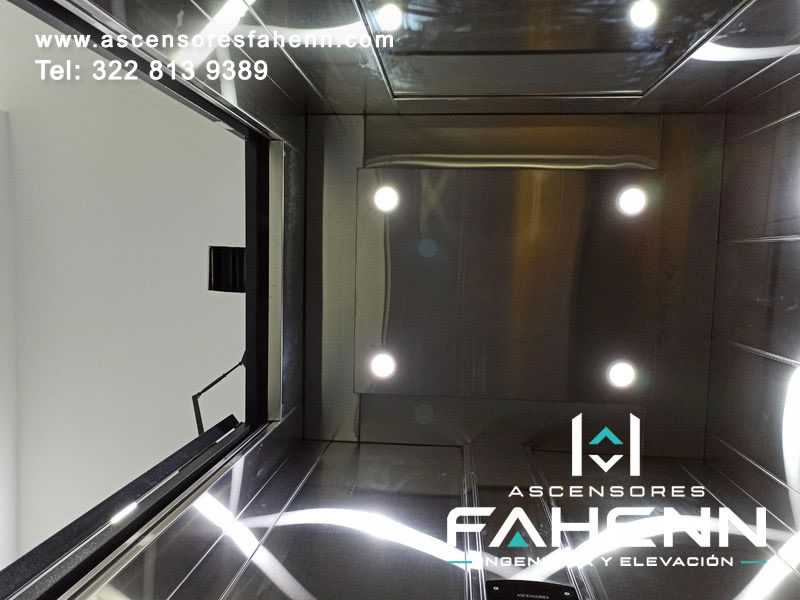 Techo de cabina de ascensor con espejos oscuros, panel central rectangular y luces LED circulares.