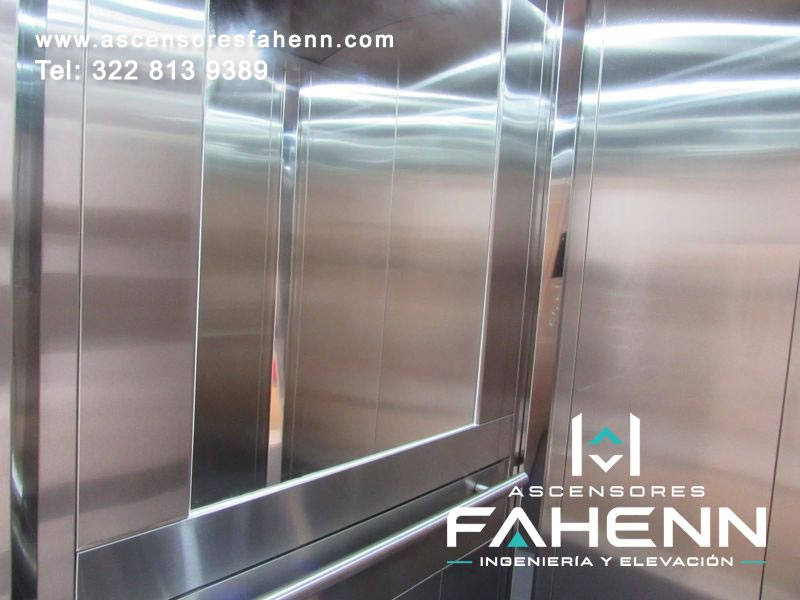 Ascensor residencial con cabina de acero inoxidable, espejo amplio, pasamanos horizontal e iluminación LED.