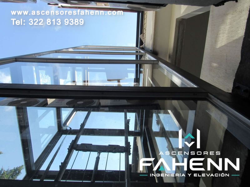 Elevador panorámico exterior con torre acristalada y estructura vertical diseñada para conectar pisos, aprovechar la luz natural y modernizar un edificio residencial.