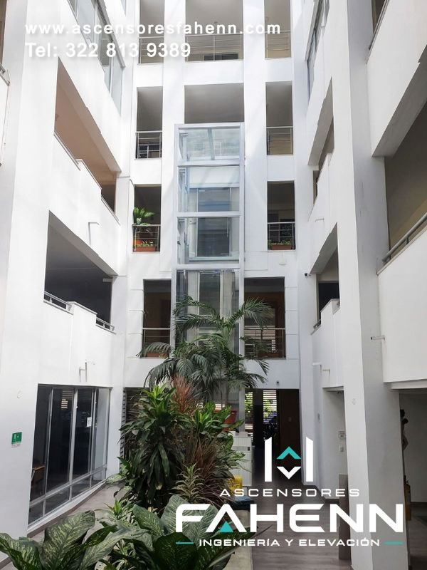 Ascensor residencial instalado en una torre de vidrio dentro de un patio central, diseñado para conectar niveles sin restar iluminación ni amplitud al edificio.