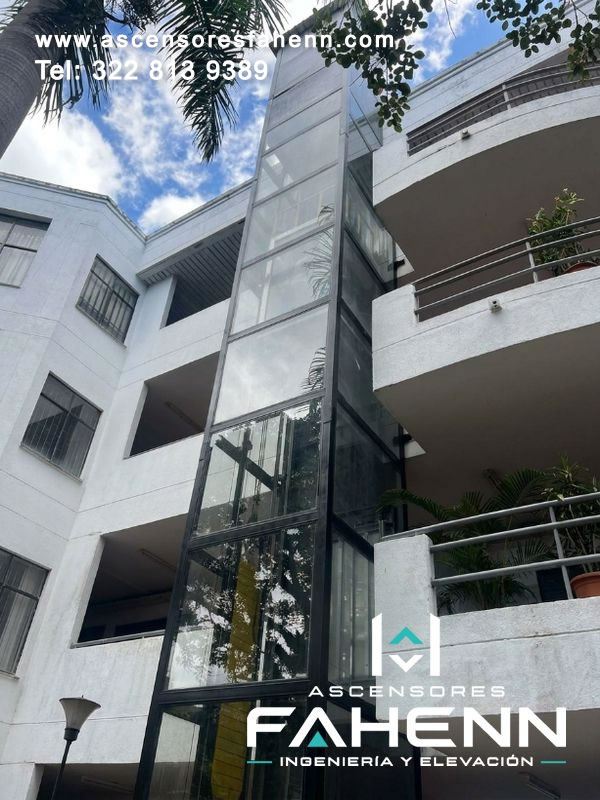 Ascensor residencial con torre exterior acristalada junto a balcones, diseñado para conectar varios pisos y mantener iluminación, visibilidad y amplitud arquitectónica.