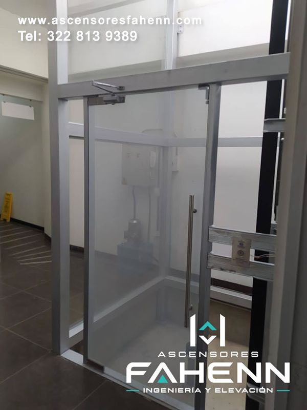 Plataforma elevadora para movilidad reducida con puerta de vidrio y entrada accesible que brinda visibilidad y protección en Bogotá, Colombia.
